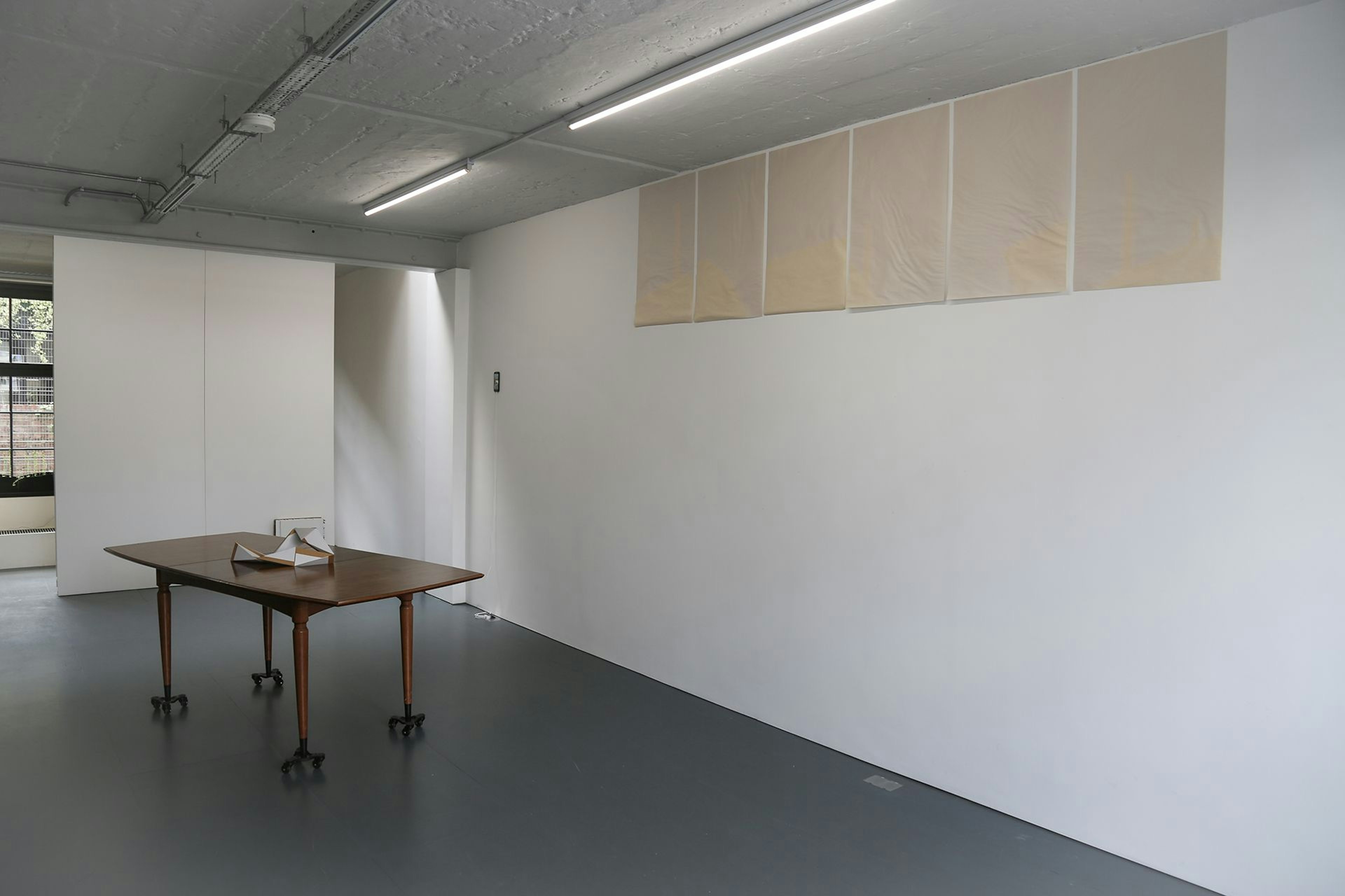 Installation view of Lucy Gunning exhibition with hanging sheets of light stencilled paper and table on wheels